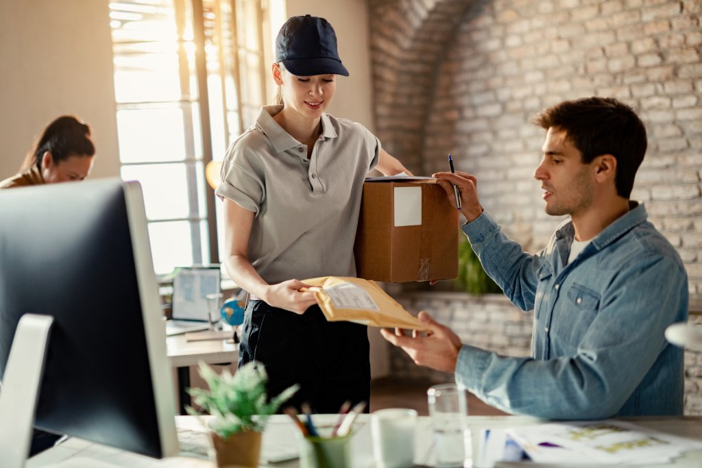 smiling female courier delivering package businessman while he is working office scaled